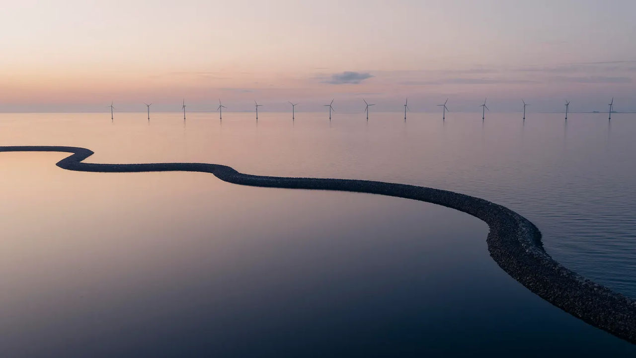 Serene sunset landscape with wind turbines reflected in calm water, backdrop for Volvo Financial Services' newsletter subscription form